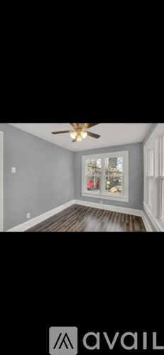 A room with a ceiling fan and a window with a view of trees and a house.