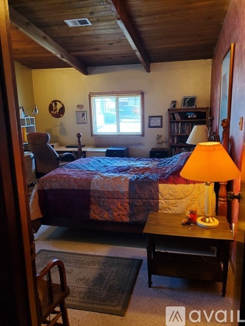 A bedroom with a bed, a chair, a lamp, and a window.