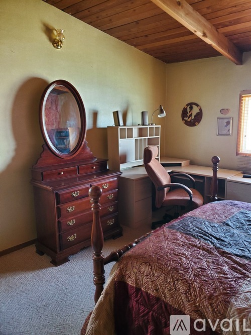 A bedroom with a bed, desk, chair, and a wooden chest of drawers.