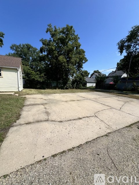 A driveway leads to a white house with a tree in the background.
