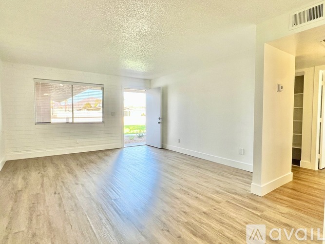 A spacious room with wooden flooring and a window with blinds.