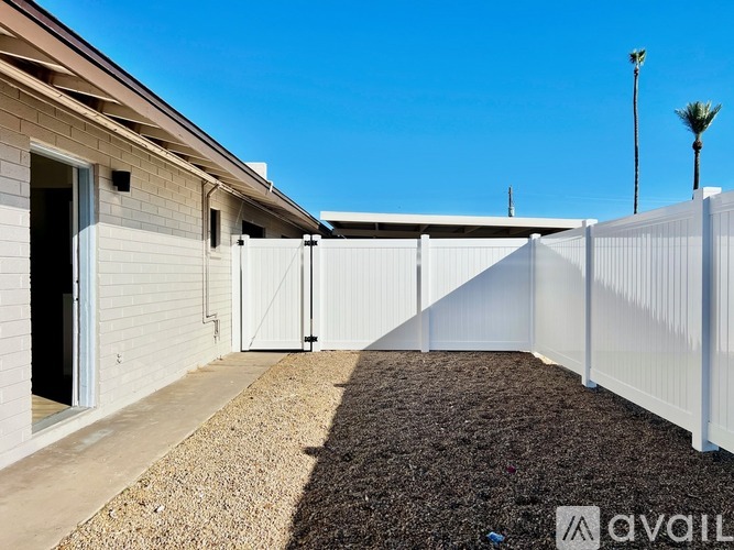 A white fence separates a gravel area from a building with a brown roof.