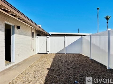 A white fence separates a gravel area from a building with a brown roof.