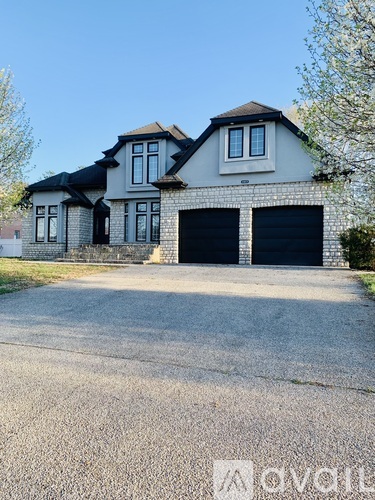 A two-story house with a black garage door is situated on a gravel driveway.