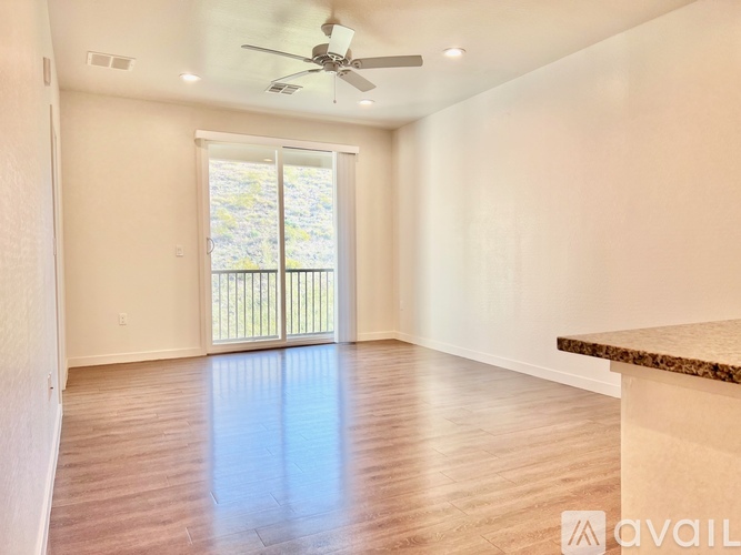 A spacious room with a ceiling fan and sliding glass doors leading to a balcony.