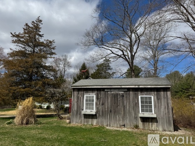 A shed sits in a grassy field with trees in the background.