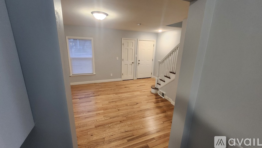 A room with wooden flooring and white walls, with a window and a door visible.