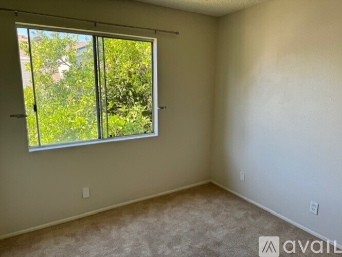 A room with a carpeted floor and a window with a view of trees and a house.