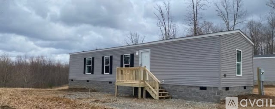 A grey mobile home with a wooden deck and a sign that says "available".