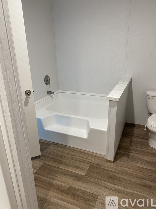A white bathroom with a tub, toilet, and wooden floor.