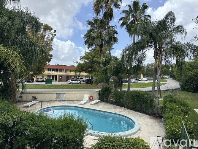 A pool surrounded by trees and bushes with a building in the background.