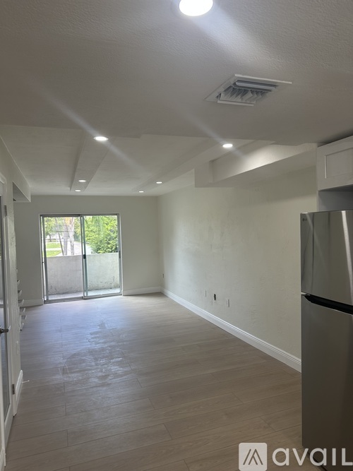 A spacious room with wooden flooring and a sliding glass door leading outside.