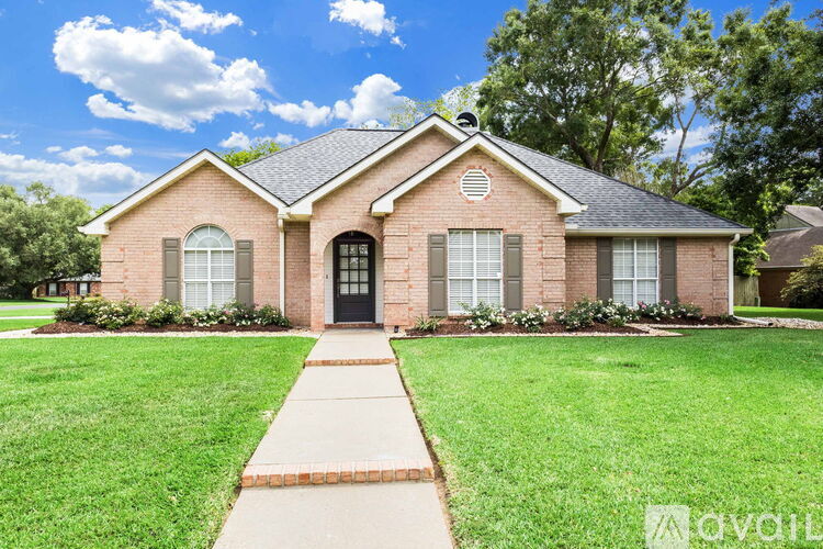 A brick house with a black door and windows is surrounded by a green lawn.
