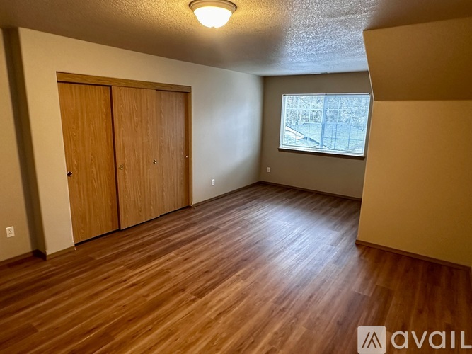 A room with wooden floors and a window showing a view of a fence and trees.