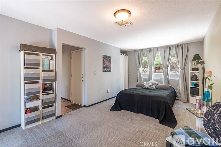 A bedroom with a bed, a window with curtains, and a bookshelf.