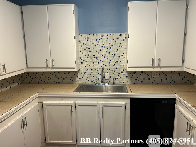 A kitchen with white cabinets and a blue backsplash.