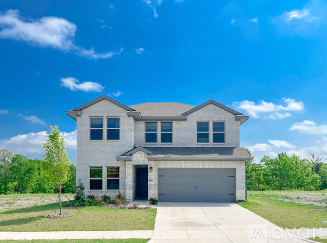 A two-story house with a garage is surrounded by a grassy area and trees.