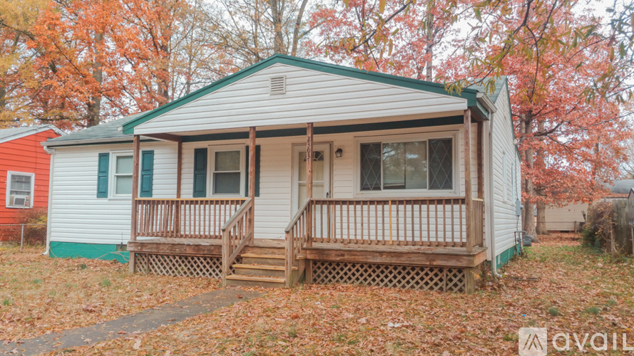 A small house with a porch and a green roof surrounded by trees with orange leaves.