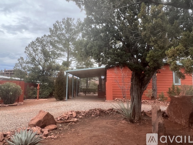 A red house with a gravel driveway and trees in the background.