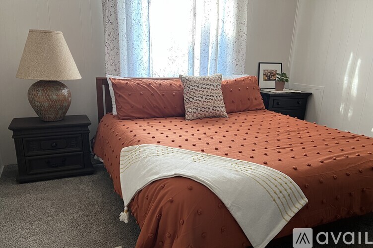 A bedroom with a bed covered in orange bedspread and a lamp on a side table.