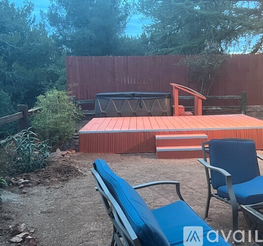 A backyard with a hot tub, chairs, and a wooden deck.