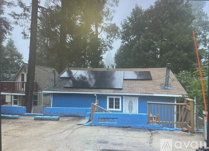A blue house with a brown roof and a white door is surrounded by trees.