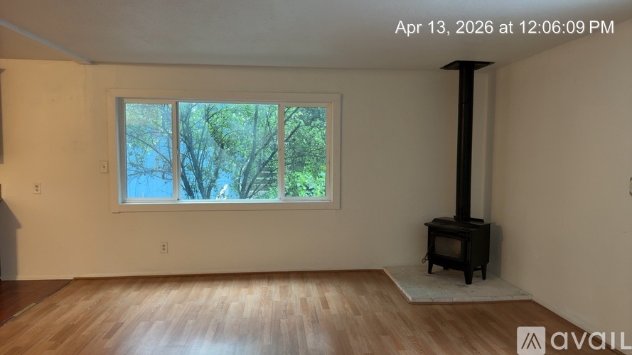 A room with a wood floor, a window, and a wood stove.