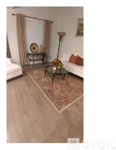 A living room with a white couch, a glass coffee table, and a rug.