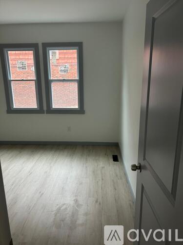 A room with a grey door and two windows with a brick wall visible through the windows.
