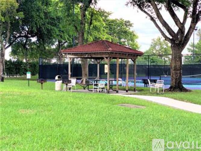 A gazebo is surrounded by trees and a fence in a grassy area.