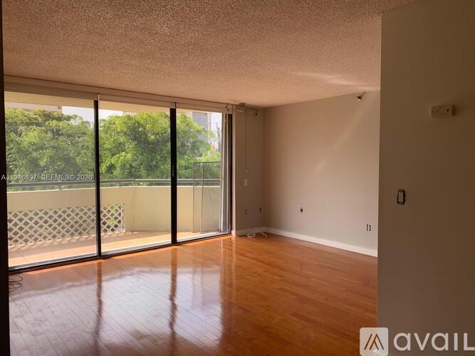 A room with wooden floors and a large window with a view of trees.