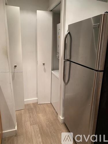 A stainless steel refrigerator in a kitchen with wooden flooring.
