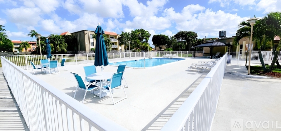 A pool surrounded by a white fence with blue chairs and umbrellas.
