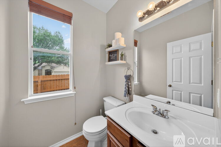 A bathroom with a white toilet, sink, and a window with a view of a fence and trees.