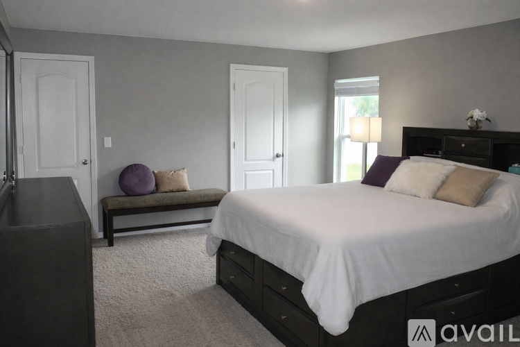 A bedroom with a large bed and a bench with a purple pillow.