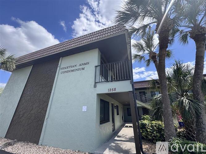 A building with the sign "Venetian Arms Condominium" is surrounded by palm trees.