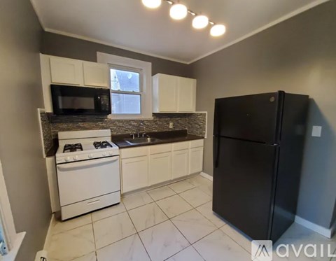 A kitchen with a black refrigerator, white cabinets, and a tiled floor.