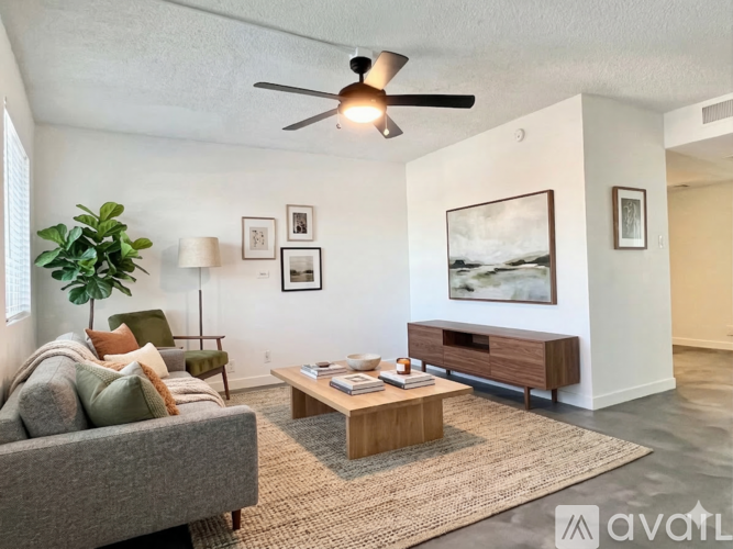A living room with a grey couch, a wooden coffee table, a ceiling fan, and a large painting on the wall.