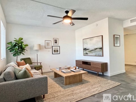 A living room with a grey couch, a wooden coffee table, a ceiling fan, and a large painting on the wall.