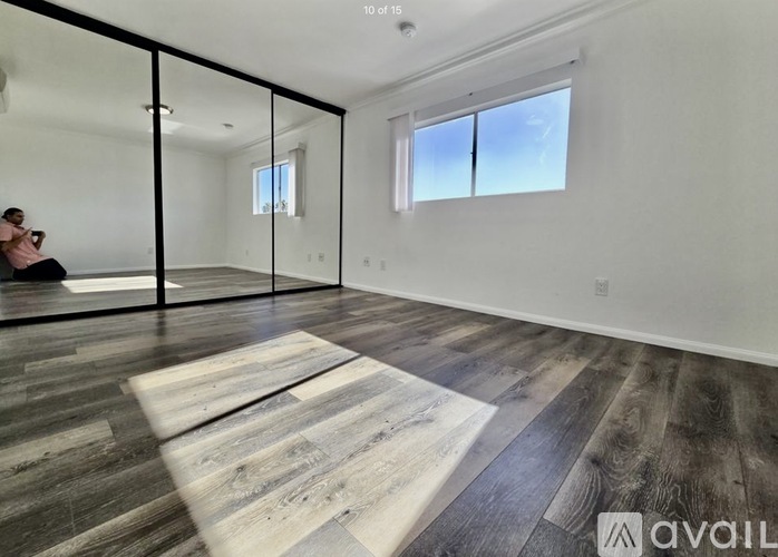 A woman is sitting on a wooden bench in a spacious room with a large mirror and wooden flooring.