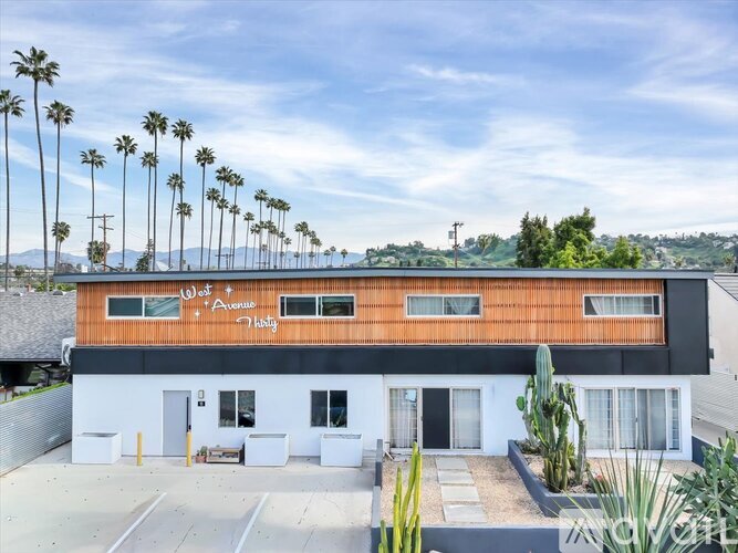A building with a brown roof and a sign that says "W 1 Avenue" is surrounded by palm trees.