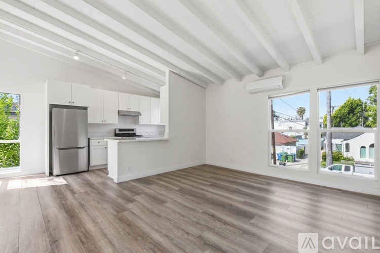 A spacious, empty room with a kitchen area and a view of the outdoors through the windows.
