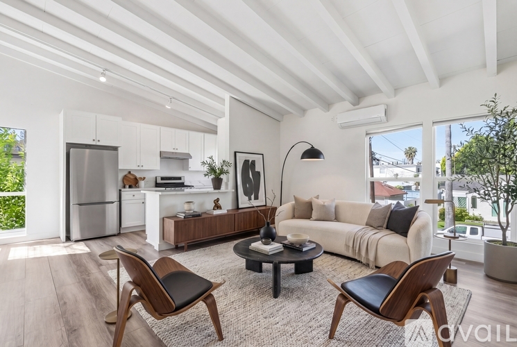 A modern living room with a white sofa, wooden chairs, and a coffee table.
