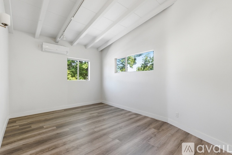 A spacious room with wooden flooring and two windows.