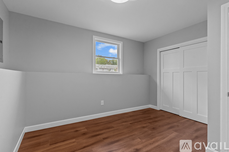 A room with wooden flooring and a window showing a view of trees and a house.