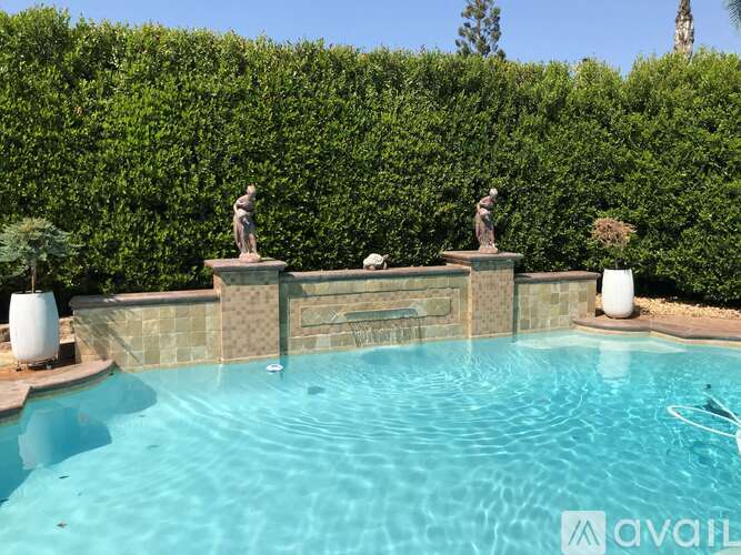 A pool surrounded by a hedge with two statues on the side.