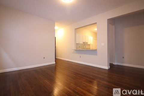 A room with wooden floors and a mirror reflecting a kitchen.