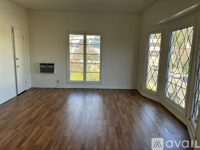 A room with wooden flooring and a window with a view of a building.