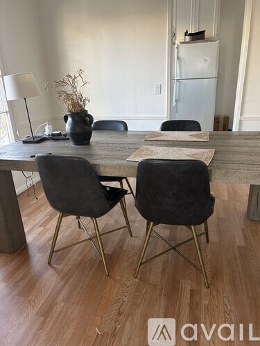 A dining room with a table, chairs, and a vase of dried flowers.