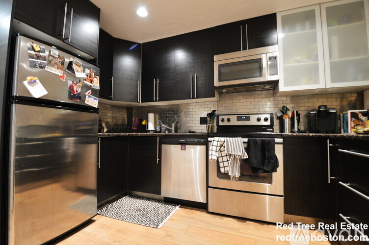 A kitchen with black cabinets and a stainless steel refrigerator.